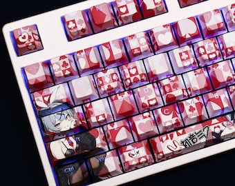 May include: A white mechanical keyboard with custom keycaps featuring red and white playing card suit designs. Some keycaps have anime-style illustrations. The keyboard has a blue backlight.