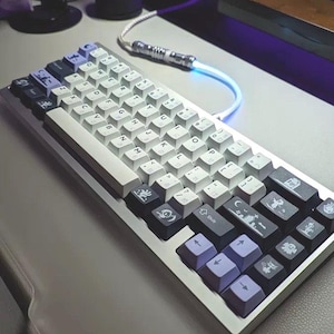 May include: A white and grey mechanical keyboard with custom keycaps featuring various symbols and designs. The keyboard has a silver frame and a white and grey cable.