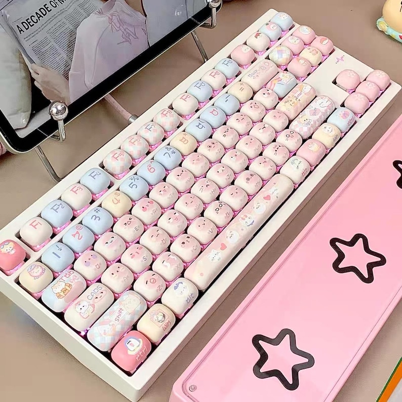 May include: A white keyboard with pink and blue keycaps featuring cartoon animal designs. The keyboard has a white frame and a pink and white cable. The keycaps have a variety of designs, including a cat, a dog, a rabbit, and a bear.