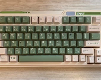 Könnte beinhalten: Eine weiße und grüne Tastatur mit japanischen Zeichen und dem Text "Kzzi" und "クリーム抹茶" auf den Tasten. Die Tastatur hat einen cremefarbenen Rahmen und grüne Akzente.