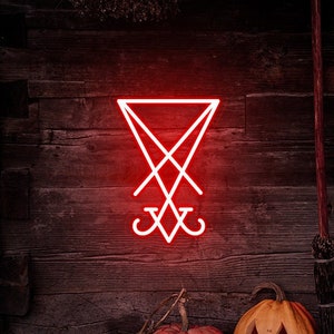 May include: A red neon sign depicting the sigil of Satan, a pentagram with an inverted cross, on a dark wooden wall. Two carved pumpkins sit in front of the sign, one with a traditional jack-o'-lantern face and the other with a more sinister expression. A broom leans against the wall.