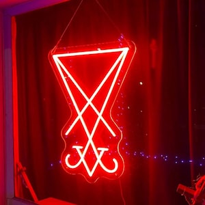 May include: A red neon sign in the shape of a pentagram with a cross inside. The sign is hanging in a window.