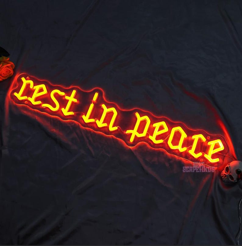 K&ouml;nnte beinhalten: Ein Neon-Schild mit den Worten "rest in peace" in einer gotischen Schriftart. Das Neon ist gelb und der Hintergrund ist schwarz.