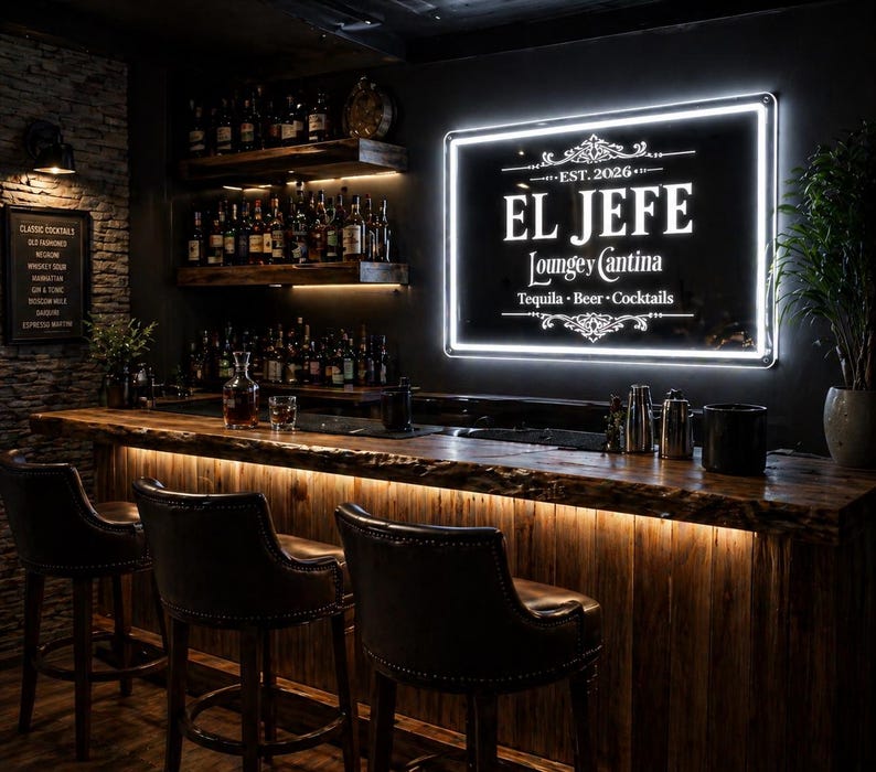 May include: A dimly lit bar with a wooden counter and three leather bar stools. A glowing sign reads "EL JEFE Lounge y Cantina" above the bar. Shelves behind the bar display bottles of liquor. A menu board lists classic cocktails.