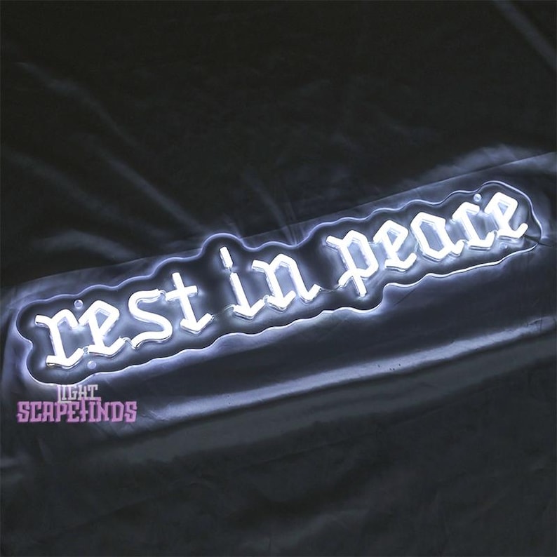 K&ouml;nnte beinhalten: Ein wei&szlig;es Neon-Schild mit den Worten "rest in peace" in gotischer Schrift.