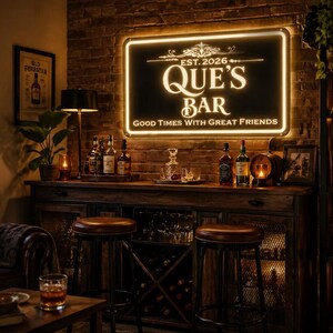 May include: A dimly lit bar scene with a sign that reads "QUE'S BAR" and "GOOD TIMES WITH GREAT FRIENDS." The bar features a wooden cabinet, stools, and various bottles of liquor. A framed picture and a small lamp are also visible.