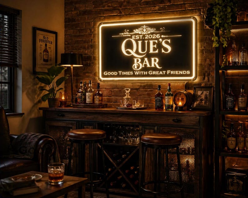 May include: A dimly lit bar scene with a sign that reads "QUE'S BAR" and "GOOD TIMES WITH GREAT FRIENDS." The bar features a wooden cabinet, stools, and various bottles of liquor. A framed picture and a small lamp are also visible.