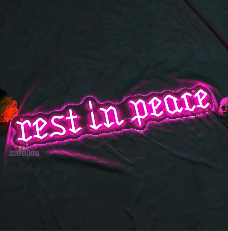K&ouml;nnte beinhalten: Pinkfarbenes Neon-Schild mit den Worten "Ruhe in Frieden" in gotischer Schrift.