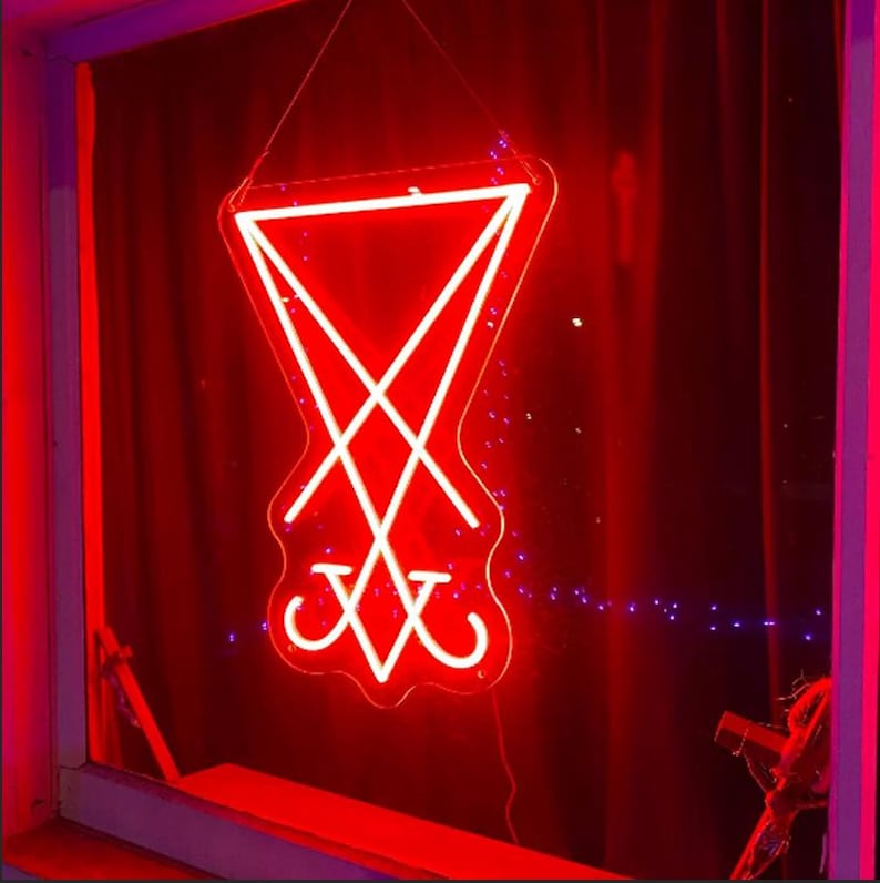 May include: A red neon sign in the shape of a pentagram with a cross inside. The sign is hanging in a window.