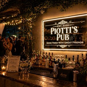 May include: Lit-up sign for Piotti's Pub, established in 2026, with the phrase "Good Times With Great Friends." The bar is stocked with bottles and glassware. A wooden bar and candles are in the foreground.