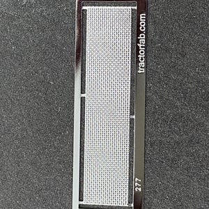 May include: A rectangular metal stencil with a grid pattern in the center. The stencil has a dark, reflective finish. The text "tractorfab.com" is printed vertically on the right side, and the number "277" is in the bottom right corner.