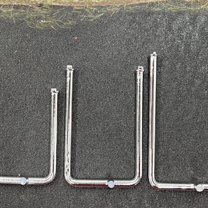 May include: Three chrome U-shaped door handles in different sizes. Each handle has a rectangular mounting plate at the top and a small, round connector at the bottom. The handles are arranged from smallest to largest.