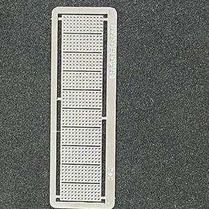 May include: A rectangular, light-colored plastic model with a grid pattern. The model has a series of rectangular sections with small, evenly spaced holes. The text "decaled.com" is printed on the side. The model is on a dark, textured surface.