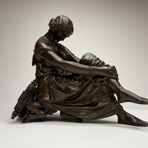 May include: A bronze sculpture of a seated woman with her leg crossed, holding her foot. The sculpture is detailed and realistic, with intricate folds in the woman's clothing.