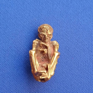 May include: A gold-colored metal figurine of a seated figure with intricate details. The figure has a crown-like headpiece and is holding a small object in its hands.