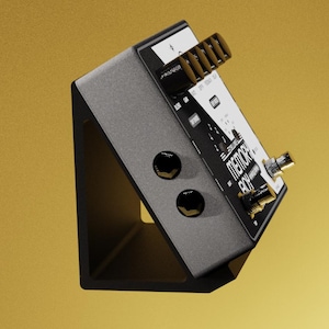 May include: A gray and black electronic device with the text "MEMORY BOY" is mounted on a black angled stand. The device has multiple knobs, buttons, and input jacks. The background is a solid gold color.