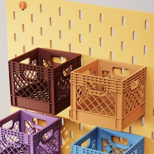 May include: Four colorful plastic milk crates in brown, orange, purple, and blue are mounted on a yellow pegboard. The crates have a rectangular shape with a lattice design and handles. The pegboard has evenly spaced slots.