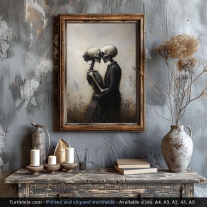 May include: A framed wall art print depicting two skeletons in an embrace, one wearing a dark suit and the other a dress, set against a muted, hazy background. The artwork is displayed in a wooden frame, capturing a somber, monochromatic aesthetic.