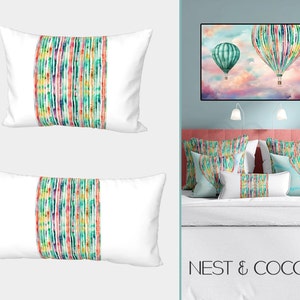 May include: Two white pillow covers featuring a colourful abstract design. The design incorporates vertical stripes in various shades of green, blue, pink, and yellow. The pillows are displayed on a bed with a white duvet cover and a light blue wall behind the bed. The text "NEST & COCOON" is visible at the bottom of the image.