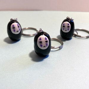 Puede incluir: Tres llaveros negros con anillas de plata. Cada llavero presenta una cara blanca con detalles morados, que se asemeja al personaje Sin Cara de la pel&iacute;cula animada El viaje de Chihiro.