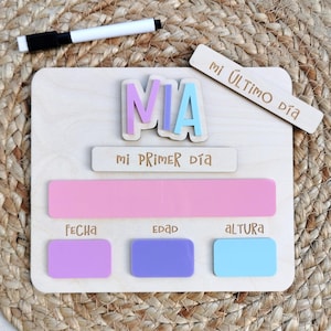 Könnte beinhalten: Ein helles Holz-Meilensteintafel mit dem Namen MIA in violetten und blauen Acrylbuchstaben. Es enthält gravierte Texte mi PRIMER DÍA, mi ÚLTIMO DÍA, FECHA, EDAD, aLTURa sowie rosa, violette und blaue Acrylrechtecke und einen schwarzen Marker.