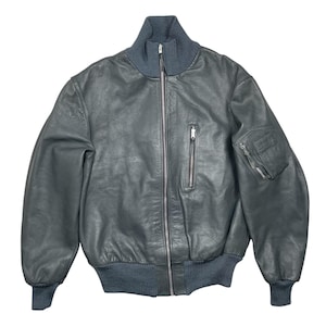 Puede incluir: Chaqueta bomber de cuero gris oscuro con cuello, puños y cintura de canalé. La chaqueta tiene una cremallera frontal, un bolsillo en el pecho con cremallera y un bolsillo en la manga izquierda. Estilo clásico y vintage.