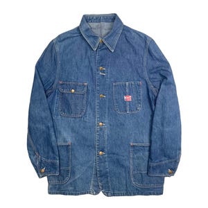 May include: A blue denim work jacket with a button-up front, two chest pockets, and two large lower pockets. The jacket has a red and white patch on the right chest pocket.