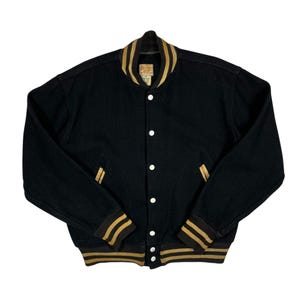 Peut inclure: Veste de style universitaire noire avec des détails rayés or et noir sur le col, les poignets et les poches. Elle possède une fermeture boutonnée avec des boutons blancs et un style classique.