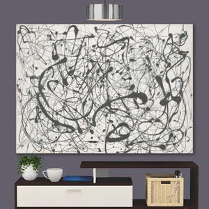 Puede incluir: Pintura abstracta en blanco y negro con fondo blanco y líneas y manchas negras. La pintura está enmarcada y colgada en una pared sobre un centro de entretenimiento blanco y marrón.