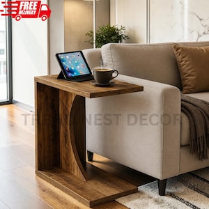 May include: A C-shaped side table with a dark wood grain finish, featuring a flat top surface, a curved vertical support panel, and a rectangular base. A tablet and a dark ceramic mug are placed on the top surface of the wooden side table.
