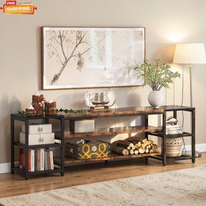Può includere: Un mobile TV a più ripiani con struttura in metallo scuro e piano effetto legno. Il mobile presenta ripiani aperti per riporre e mostrare oggetti, con elementi decorativi come libri, scatole e un vaso. Un'opera d'arte incorniciata è appesa sopra.