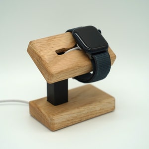 Könnte beinhalten: Ein Holzlade-Ständer für eine Apple Watch mit einem schwarzen Ladekabel. Der Ständer hat eine schwarze Basis und einen Schlitz für das Armband der Uhr.