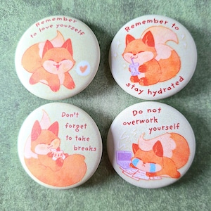 Può includere: Quattro bottoni rotondi giallo chiaro con illustrazioni di una volpe dei cartoni animati. Ogni bottone ha un messaggio diverso in testo rosso: "Remember to love yourself", "Remember to stay hydrated", "Don't forget to take breaks" e "Do not overwork yourself."