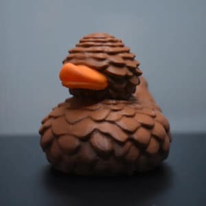May include: A brown rubber duck with a textured, pine cone-like design. The duck has an orange beak and is made to look like a pine cone.
