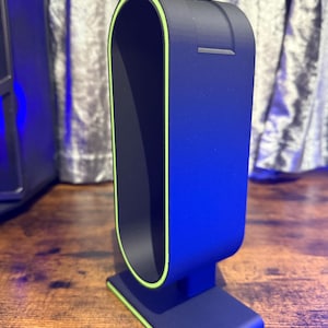 May include: A black phone stand with a green trim. The stand has a rounded top and a square base.