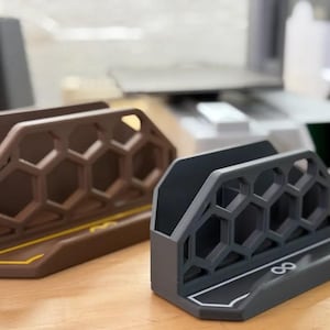 Könnte beinhalten: Zwei Desktop-Organizer aus Kunststoff mit einem Wabenmuster. Einer ist braun und der andere ist grau. Der graue Organizer hat das Unendlichkeitszeichen auf der Vorderseite.