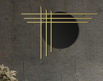 May include: A modern wall art piece featuring a black circle intersected by gold-colored lines and rectangles. The artwork hangs on a textured gray wall above a brown armchair with a white pillow. Decorative elements include pendant lights and a small side table.