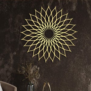 May include: A gold-coloured, laser-cut metal wall art piece in a floral design, mounted on a dark brown textured wall. The artwork is the focal point of a room with a chair, a wooden cabinet, and decorative items.