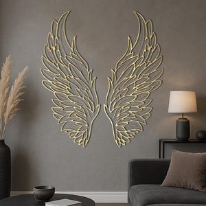Peut inclure: Une paire d'ailes d'ange dorées en décoration murale. Les ailes présentent des plumes superposées et détaillées avec un contour doré métallique. L'œuvre est fixée sur un mur gris, créant un contraste saisissant. Décoration murale.