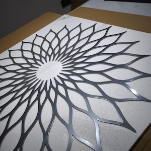 May include: A dark grey metal wall art piece with a floral design. The artwork has a central circular opening and petal-like shapes radiating outwards. It is placed on a white surface.