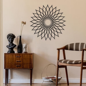 May include: A black metal floral wall art piece is mounted above a wooden cabinet in a mid-century modern style. The room features a bust, a vase, and a chair with a striped cushion. The wall is painted in a neutral tone. The cabinet is in the foreground.