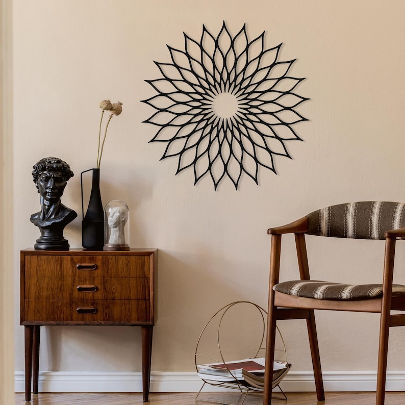 May include: A black metal floral wall art piece is mounted above a wooden cabinet in a mid-century modern style. The room features a bust, a vase, and a chair with a striped cushion. The wall is painted in a neutral tone. The cabinet is in the foreground.