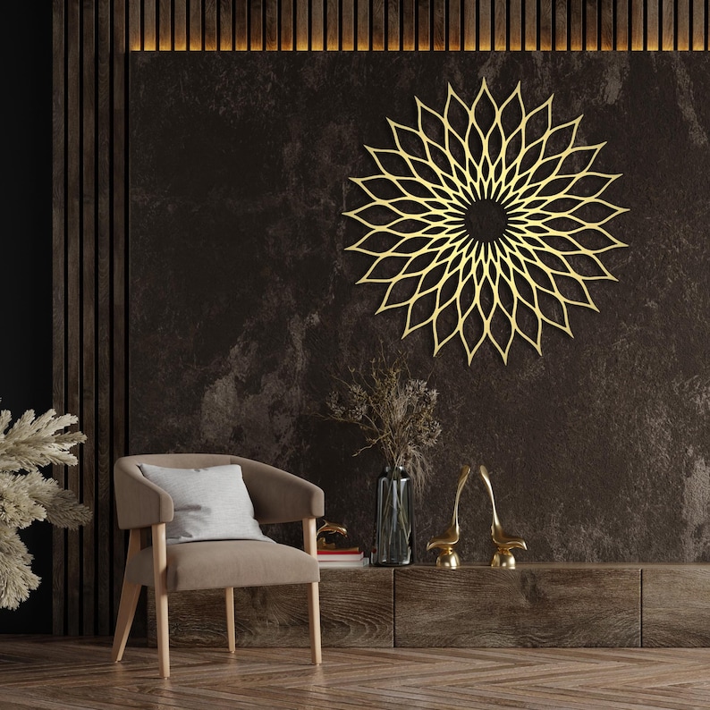 May include: A gold-coloured, laser-cut metal wall art piece in a floral design, mounted on a dark brown textured wall. The artwork is the focal point of a room with a chair, a wooden cabinet, and decorative items.