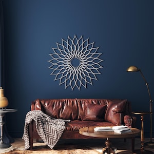 May include: A silver, flower-like wall decoration hangs on a dark blue wall above a brown leather sofa. The room includes a round wooden coffee table and a brass floor lamp. The artwork's design is a series of interconnected petal shapes.