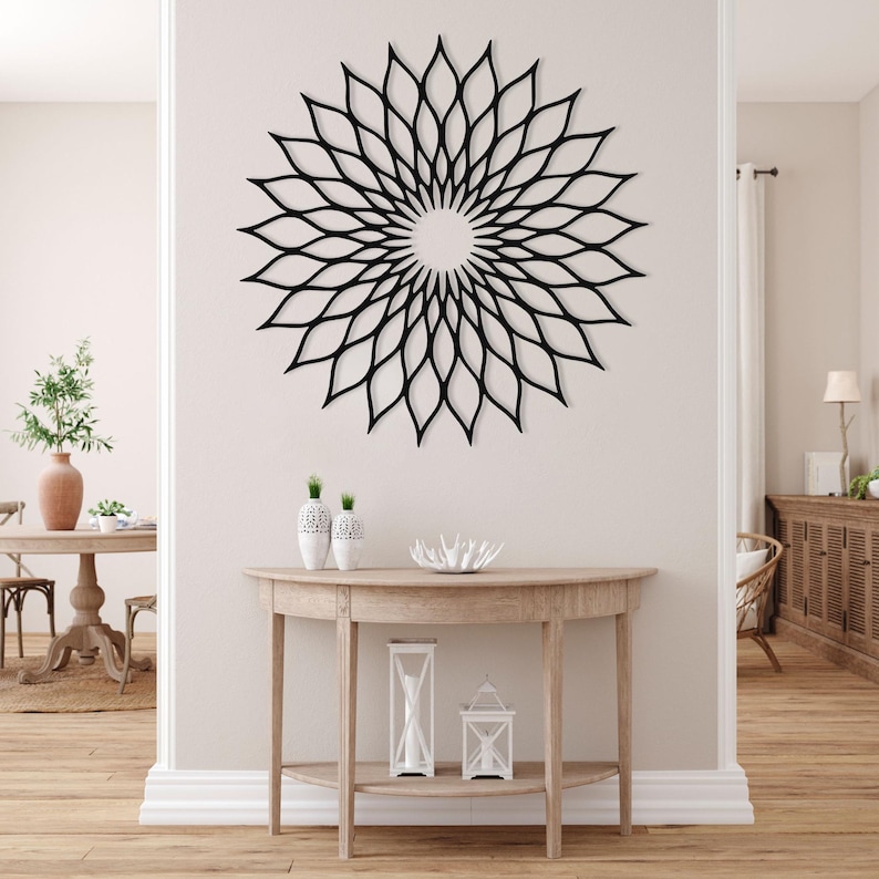 May include: A large, black, floral-shaped wall art piece with a circular design. The artwork is mounted on a light-coloured wall above a wooden console table. The table holds decorative vases and candles.