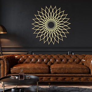 May include: A gold-coloured, circular wall art piece with a floral design is mounted on a dark wall. The artwork is above a brown leather sofa. The room has a modern, elegant aesthetic.