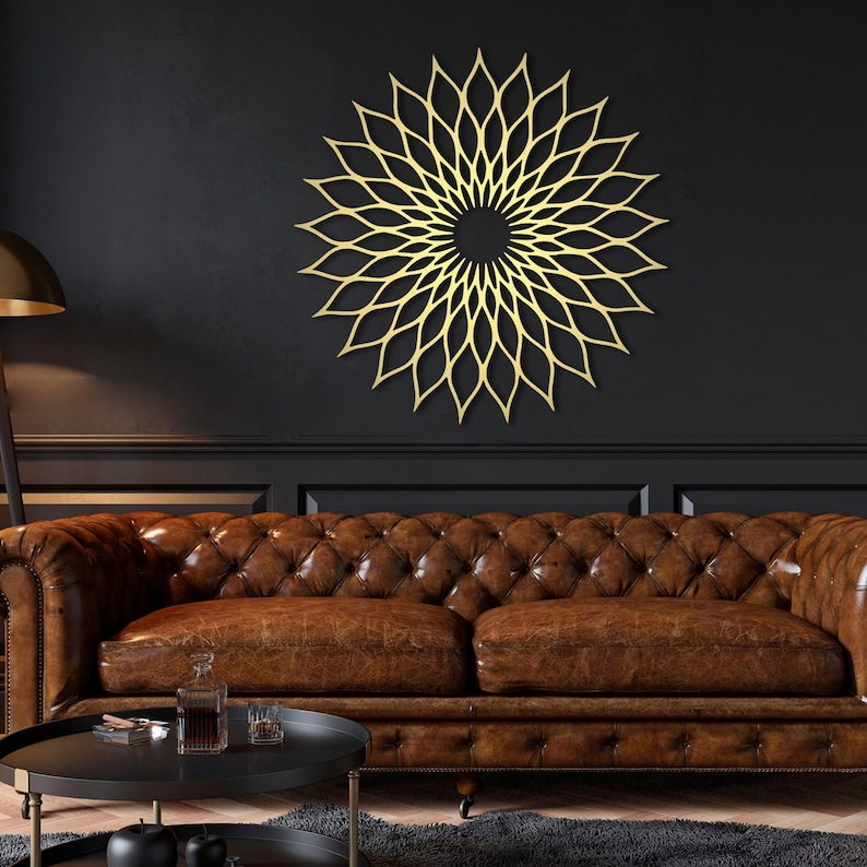 May include: A gold-coloured, circular wall art piece with a floral design is mounted on a dark wall. The artwork is above a brown leather sofa. The room has a modern, elegant aesthetic.