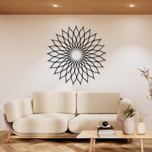 May include: A black, laser-cut metal wall art piece in a floral design, mounted on a white wall above a cream-coloured sofa. The artwork features a circular pattern of petal-like shapes radiating from a central point. The room has a modern, minimalist aesthetic.