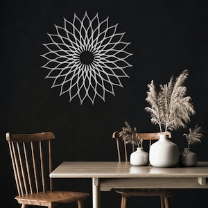 May include: A white metal wall decoration in a floral pattern is mounted on a dark wall. The artwork is the focal point of the room. A wooden table and chairs are in the foreground, with vases of dried plants.
