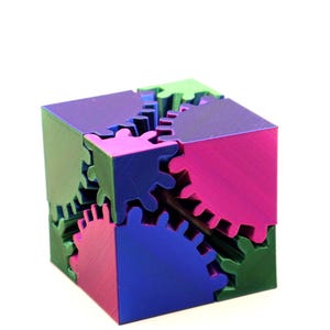 May include: A multi-coloured cube puzzle with interlocking gear-shaped pieces. The cube features vibrant hues of green, blue, purple, and pink. The puzzle is designed to fit together, showcasing a unique geometric design.